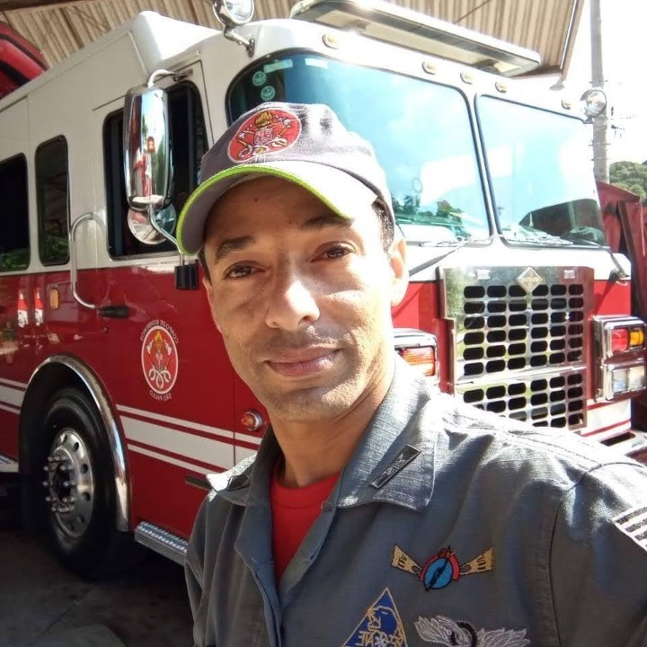 Homem com uniforme de bombeiro ao lado de um caminhão do bombeiro